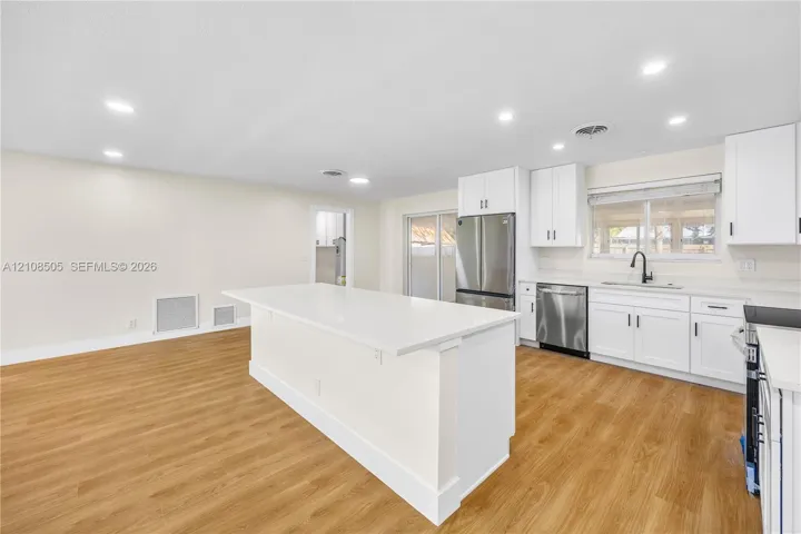 Kitchen featuring white cabinetry, quartz countertops, a central island, stainless steel appliances, and wood-finish flooring