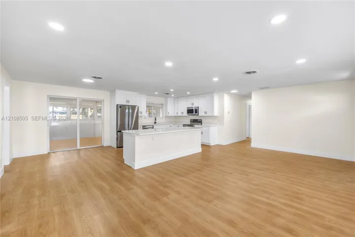Open-concept kitchen featuring white shaker-style cabinetry, quartz countertops, a center island, stainless steel appliances, and wood-finish flooring
