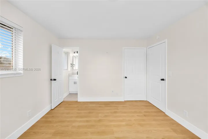 Room featuring wood-finish flooring, two white panel doors, and window with horizontal blinds