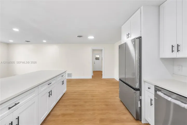 Kitchen featuring white shaker-style cabinetry, solid-surface countertops, wood-finish flooring, and stainless steel appliances