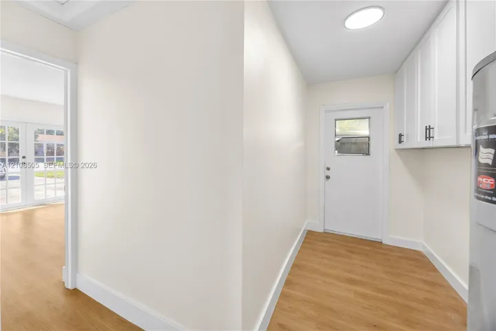 Neutral-toned interior space featuring wood-finish flooring, white shaker-style wall cabinetry with dark hardware, a recessed ceiling light, and an exterior door with a window inset