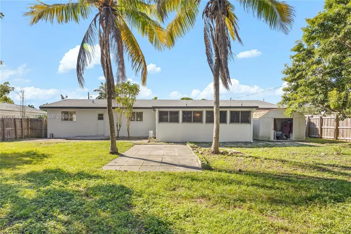 Spacious backyard featuring a grass lawn, paved patio, mature palm trees, detached storage structure, and wood privacy fencing
