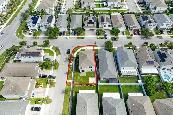 Aerial perspective of a corner lot property featuring a hip roof, paved driveway, dedicated rear patio, and expansive side lawn