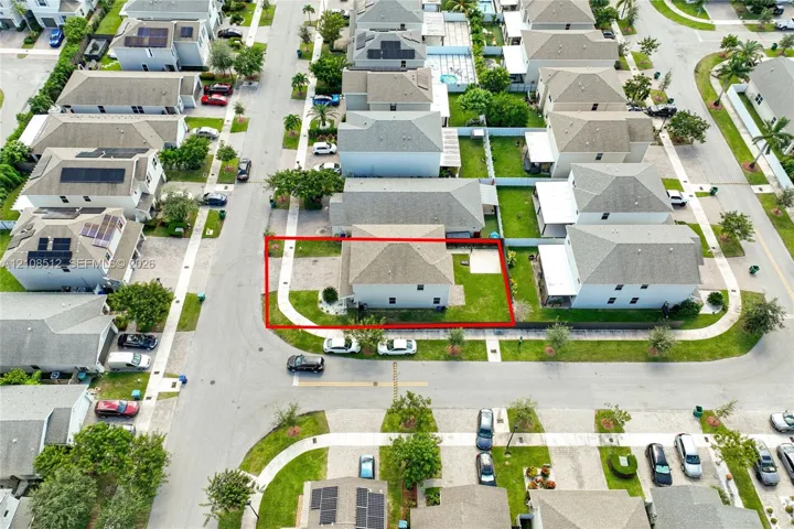 Aerial view of a corner lot property featuring a hip roof, exterior concrete walkway, paved ground-level patio, and lawn space