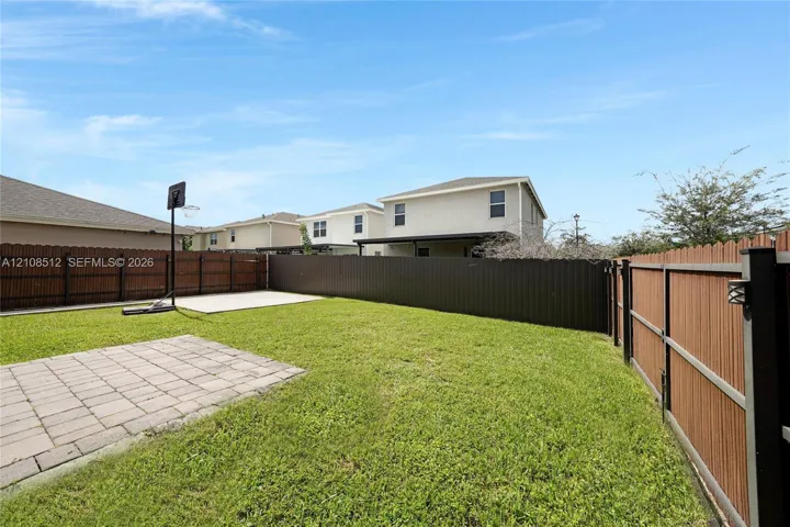 Fenced backyard featuring a manicured lawn, concrete patio, and a dedicated concrete play area