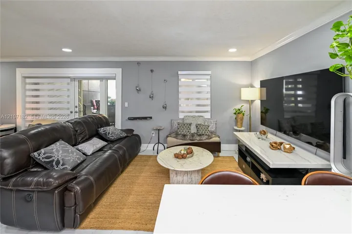 Living area featuring crown molding, recessed lighting, neutral wall paint, and sliding glass doors with roller shades