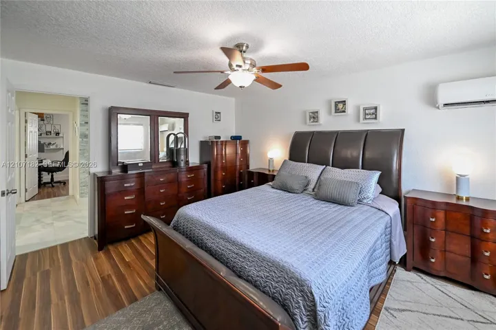 Room featuring wood-finish flooring, a wall-mounted ductless air conditioning unit, and a ceiling fan with integrated lighting
