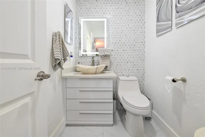 Bathroom featuring a stone vessel sink, white vanity with integrated cabinetry, mosaic tile wall accent, and illuminated vanity mirror