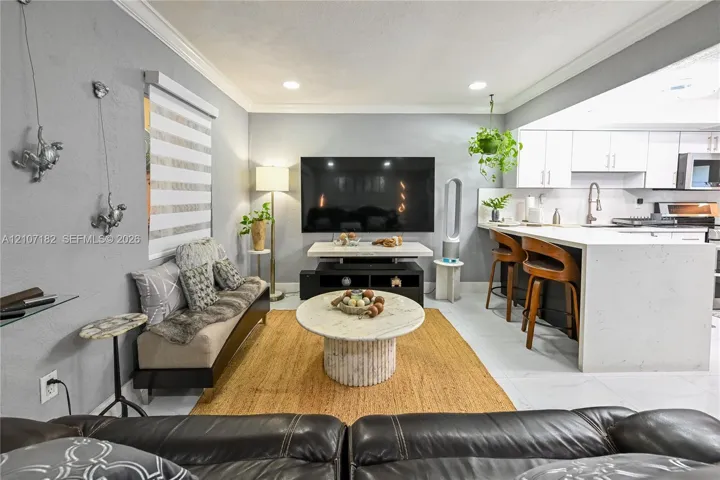 Open-concept area featuring recessed ceiling lighting, crown molding, white shaker-style cabinetry, a stone-finish waterfall edge kitchen island, and tile flooring