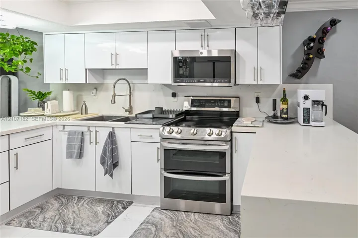 Kitchen featuring white slab-front cabinetry, light-toned quartz countertops, stainless steel dual-oven range, integrated microwave, and a high-arch gooseneck faucet