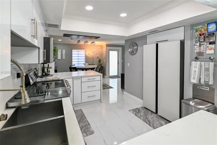 Kitchen featuring white gloss cabinetry, stone-finish countertops, large-format tile flooring, recessed lighting, and a dual-basin undermount sink with a high-arc pull-down faucet