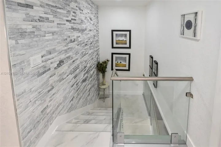 Staircase featuring stacked stone accent wall, large-format tile flooring, and glass panel railing with a metallic handrail