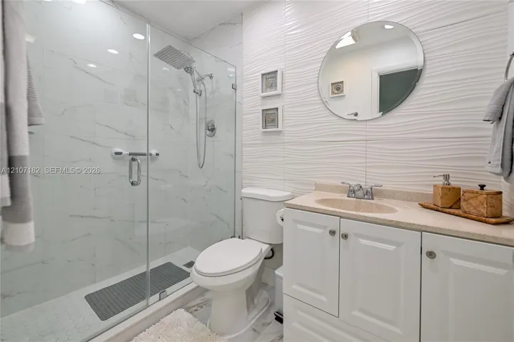 Bathroom featuring a glass-enclosed shower with a rainfall showerhead, white vanity cabinet, solid-surface countertop with an integrated sink, and textured wall tile