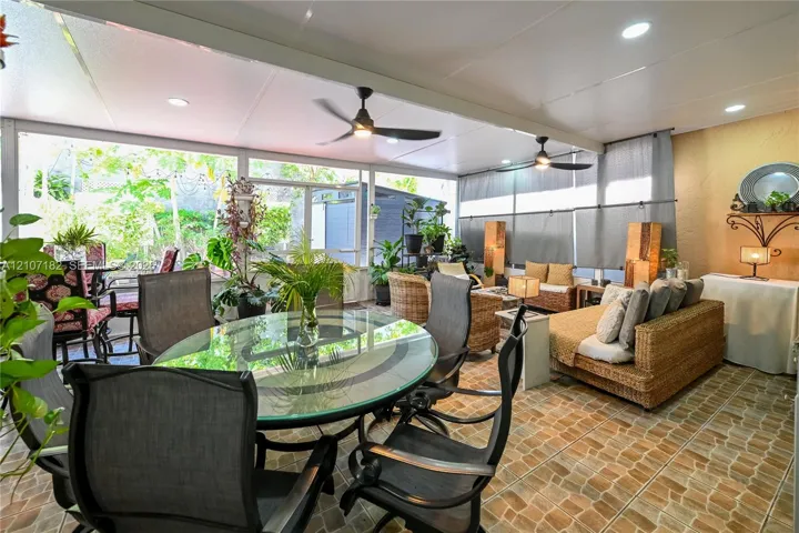 Enclosed patio featuring stone-pattern flooring, integrated ceiling lighting, dual ceiling fans, and expansive glass pane enclosures