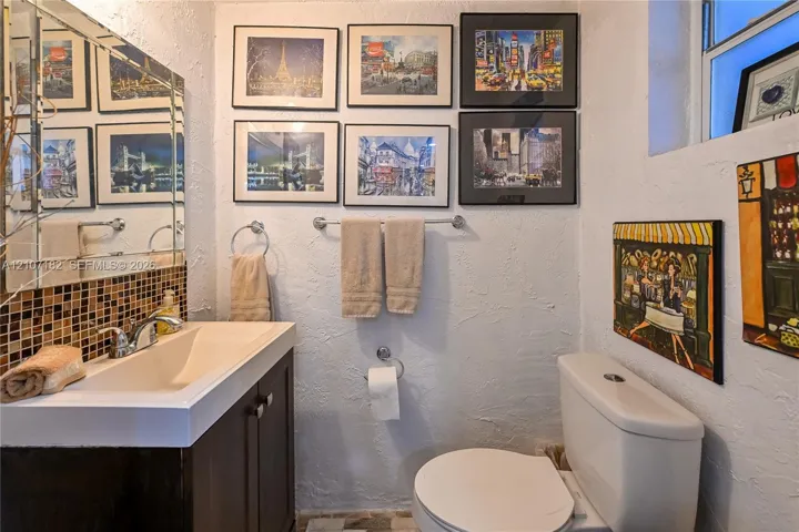 Bathroom featuring a dark-finish vanity with a rectangular integrated sink, chrome-finish faucet, multi-colored square mosaic tile backsplash, and large wall-mounted mirror