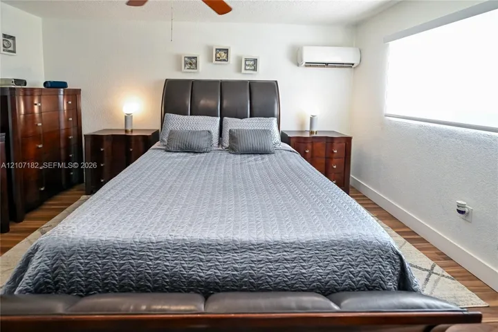 Wall-mounted air conditioning unit, wood-finish flooring, and large window with roller shade