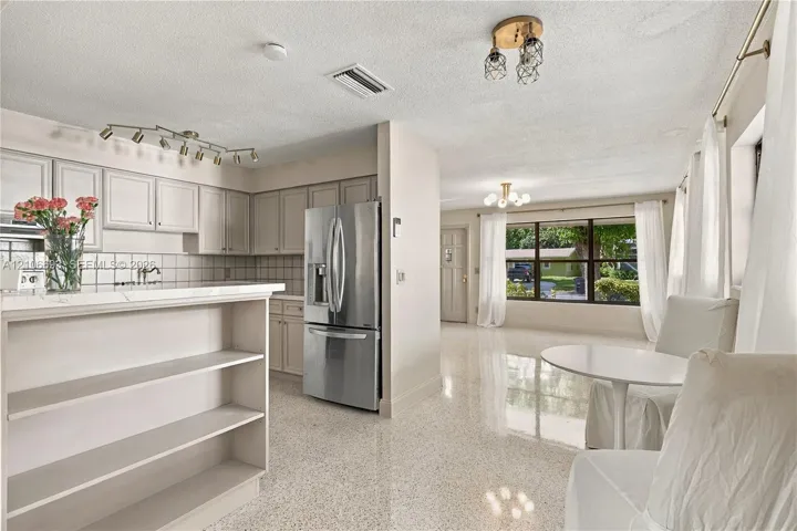 Kitchen featuring white cabinetry, stainless steel refrigerator, tile backsplash, multi-bulb track lighting, and terrazzo flooring