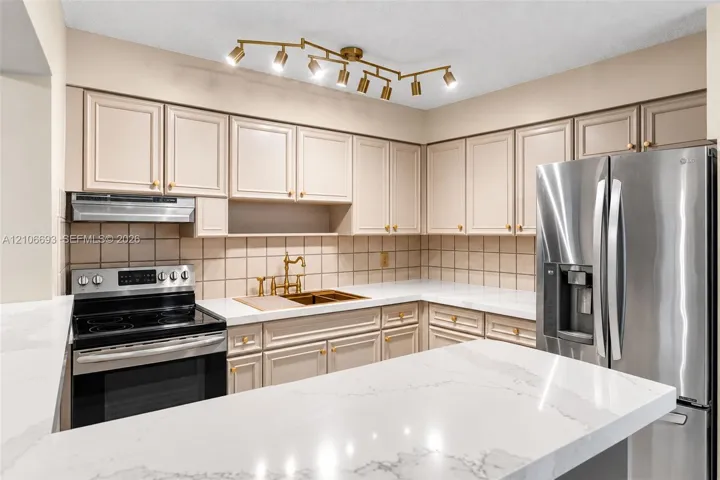 Kitchen featuring quartz countertops, shaker-style cabinetry, a multi-light directional ceiling fixture, stainless steel appliances, and a tiled backsplash
