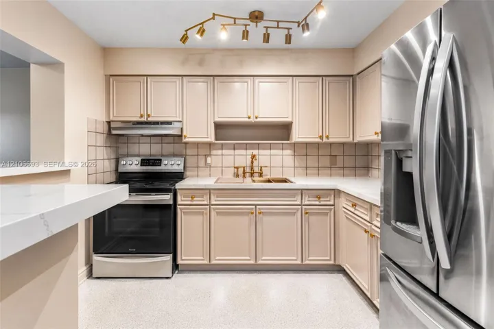Kitchen featuring custom-color cabinetry, stainless steel appliances, stone-surface countertops, square-tiled backsplash, and multi-directional track lighting
