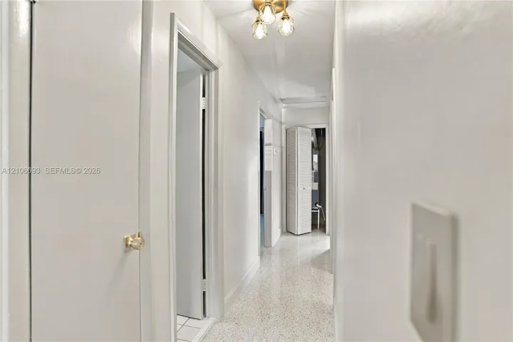 Hallway featuring neutral wall finishes, terrazzo flooring, and a multi-bulb ceiling-mounted light fixture