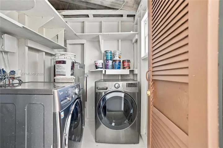 Laundry space featuring built-in open shelving, louvered door, and exposed structural framing
