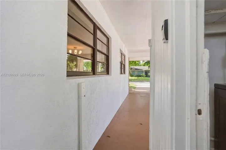 Covered exterior walkway featuring a smooth stucco finish, horizontal sliding windows with dark metal frames, and solid concrete flooring