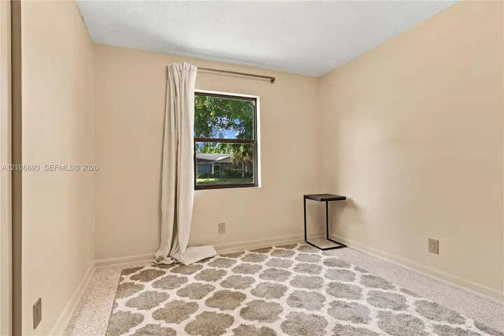 Neutral-toned room featuring a single-pane window with dark trim, textured ceiling, and terrazzo flooring
