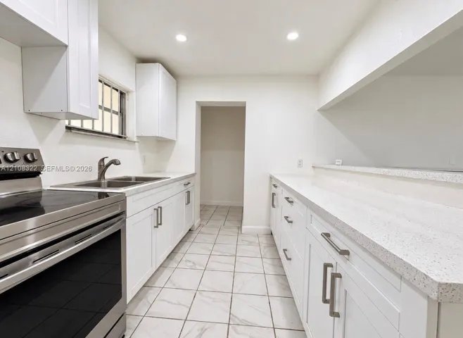 Kitchen featuring white cabinetry with brushed metal hardware, solid-surface countertops, recessed lighting, and tile flooring