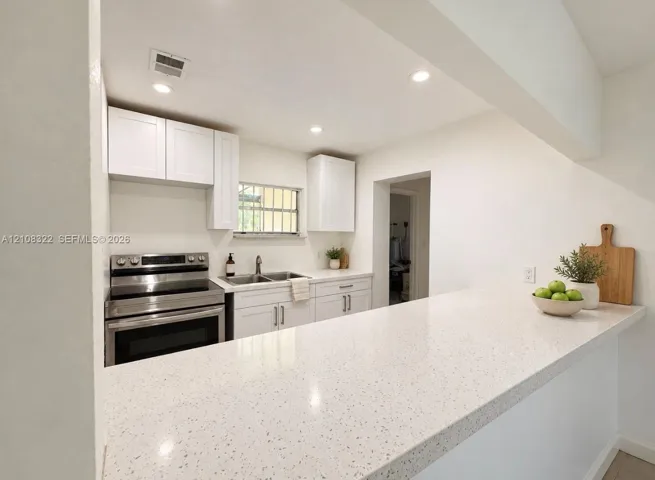 Kitchen featuring white shaker-style cabinetry, a quartz countertop breakfast bar, recessed lighting, and stainless steel appliances