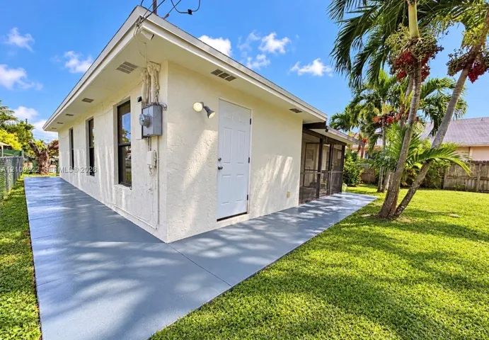 Stucco exterior featuring a wraparound concrete patio, screened-in porch, and expansive lawn with mature palm trees