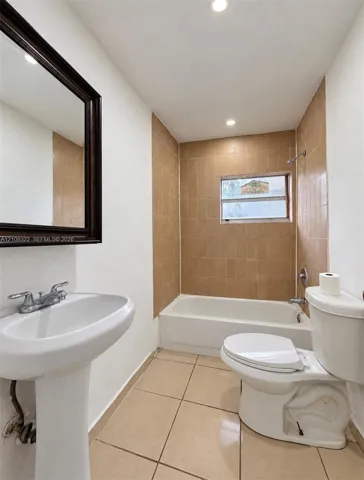 Bathroom featuring a porcelain pedestal sink, ceramic tile flooring, a shower-tub combination with tiled surround, and a framed wall-mounted mirror