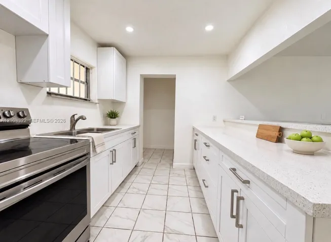 Kitchen featuring white shaker-style cabinetry, light-toned stone countertops, stainless steel range, and tile flooring