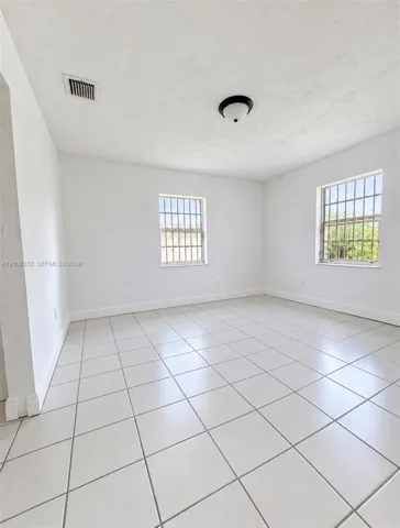 Neutral interior space featuring large-format ceramic tile flooring, two windows with metal security bars, and a central flush-mount ceiling fixture