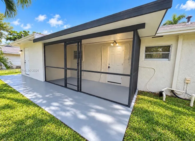 Screened-in patio with a concrete floor, exterior lighting, and painted masonry siding