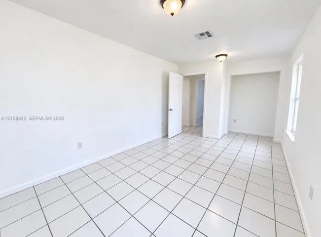 Room featuring white ceramic tile flooring, recessed wall niche, two flush-mount light fixtures, and a six-panel door