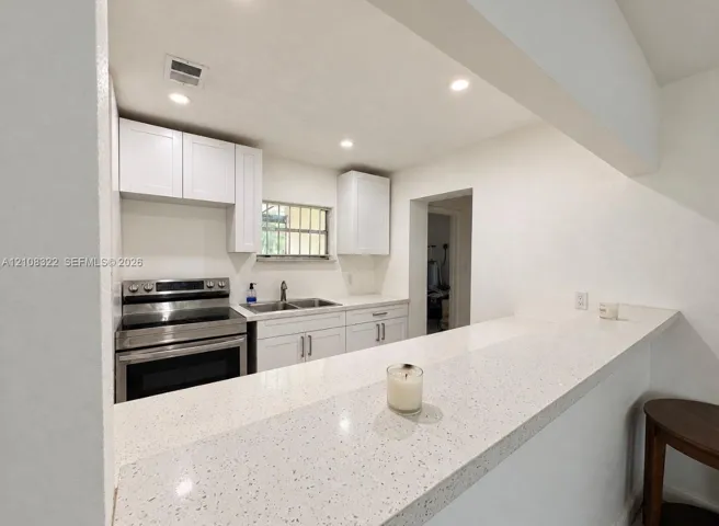 Kitchen featuring white cabinetry, quartz countertops, a dual-basin stainless steel sink, and stainless steel range