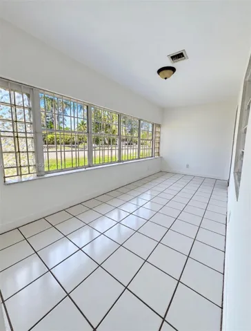 Enclosed space featuring square ceramic tile flooring, an expansive wall of multi-pane windows with metal security bars, glass block side accents, and a flush-mount ceiling light fixture