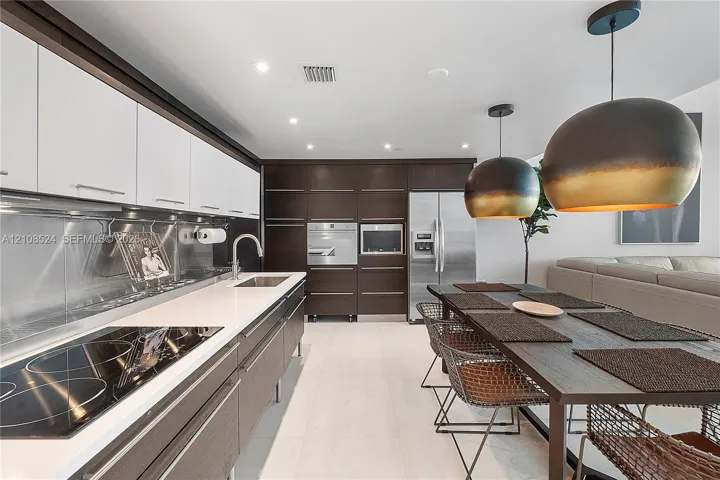 Two-tone cabinetry with white upper and dark wood-finish lower units, stainless steel backsplash, integrated wall oven and microwave, stone-finish countertops, and dual oversized dome pendant​​‌​​​​‌​​‌‌​‌‌​​​‌‌​‌​‌​‌​​​‌​​ lights