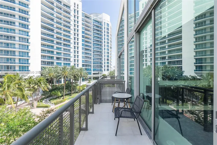 Covered balcony with large-format tile flooring, a structured metal mesh railing, and floor-to-ceiling glass panel walls