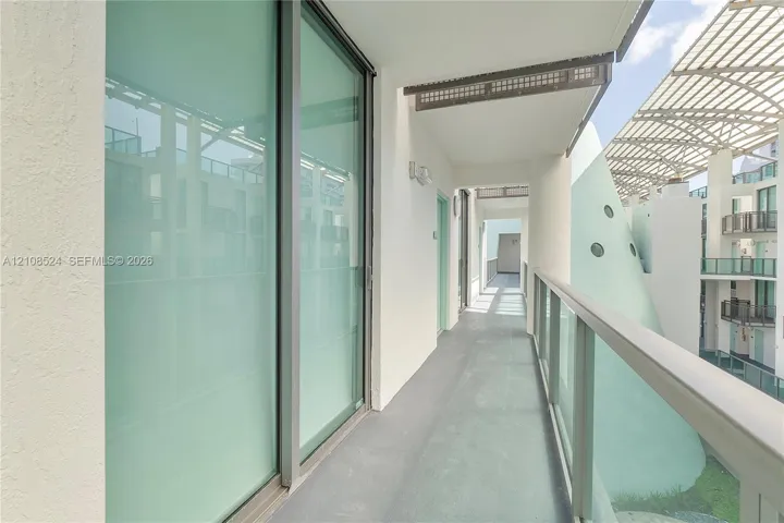 Covered balcony featuring full-height glass sliding doors, smooth concrete flooring, and a glass-panel railing