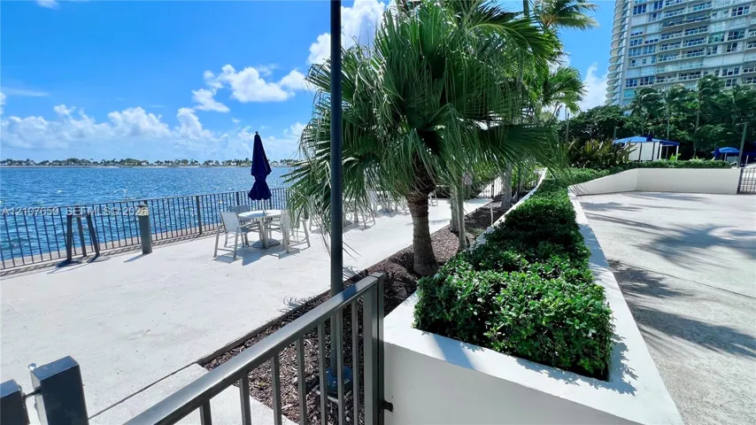 Waterfront concrete patio with metal perimeter fencing, elevated masonry landscape planters, and mature palm​​‌​​​​‌​​‌‌​‌‌​​​‌‌​‌​‌​‌​​​‌​​ trees