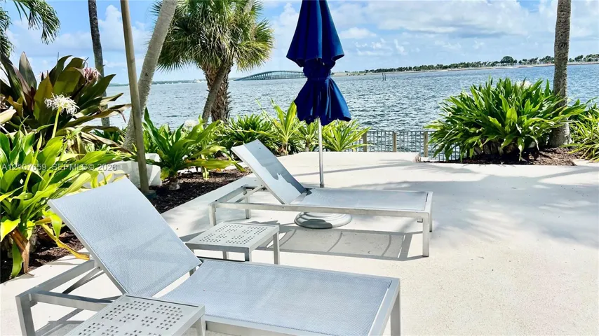 Concrete patio featuring lush tropical landscaping, mature palm trees, and waterfront positioning