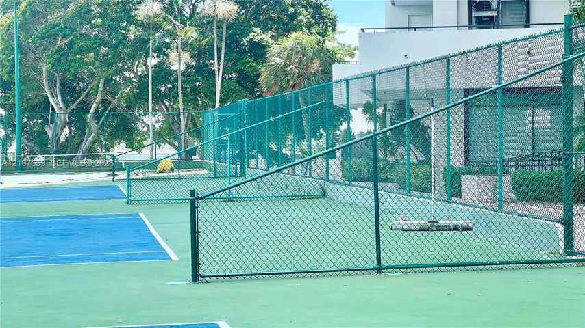 Tennis court with hard-surface playing area, perimeter chain-link fencing, and overhead court lighting