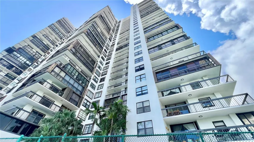 High-rise building exterior featuring private balconies with metal railings, expansive window arrays, and mature palms