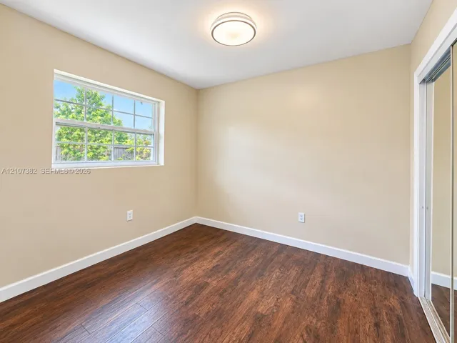 Room featuring wood-finish flooring, a multi-pane window, mirrored sliding closet doors, and a flush-mount ceiling light fixture