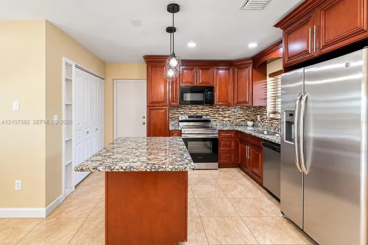 Kitchen featuring raised-panel wood cabinetry, stone countertops, stainless steel appliances, multi-toned stone tile backsplash, and ceramic tile flooring