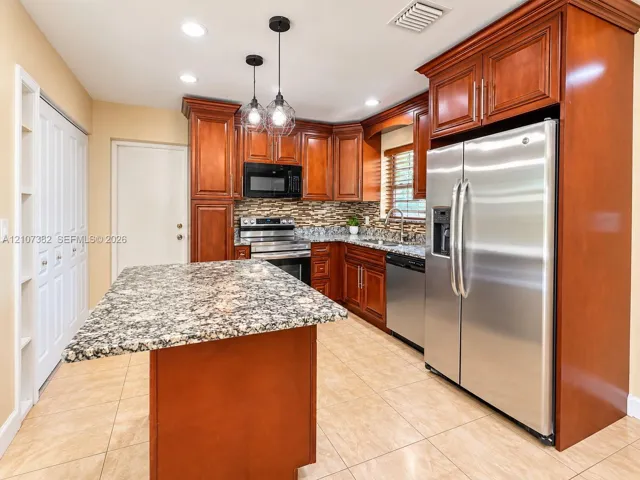 Kitchen featuring stained wood cabinetry, stone countertops, a central island, tile flooring, and stainless steel appliances