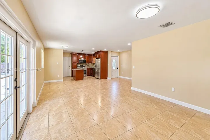 Open-concept interior featuring large-format tile flooring, recessed lighting, wood-finish cabinetry, stainless steel appliances, and glass-paned double doors