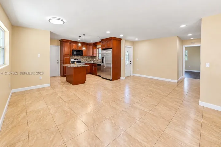 Kitchen featuring wood cabinetry, stone-finish countertops, stainless steel appliances, a center island, and neutral tile flooring