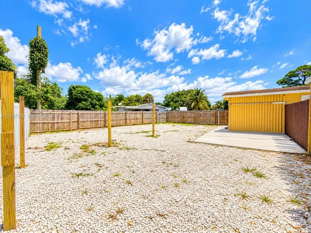 Fenced backyard featuring a gravel surface, concrete patio, and vertical wood structural posts